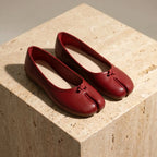 Ballerines bout fendu en cuir vegan rouge cramoisi avec nœud délicat sur bloc de pierre beige
