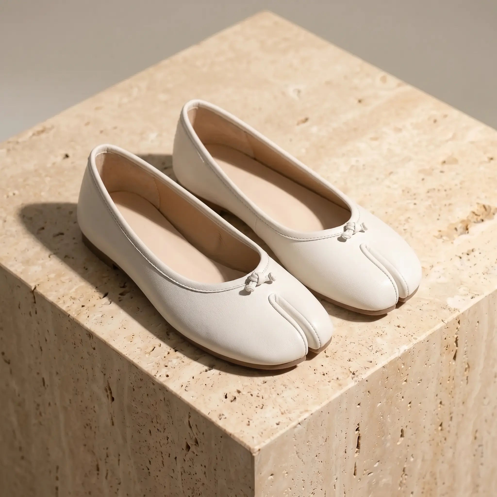 Ballerines bout fendu blanc ivoire en cuir vegan mat, vue trois-quarts sur surface claire